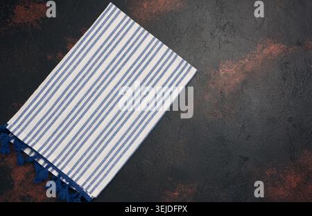 Folded linen striped kitchen towel on a black background, top view. Stock Photo