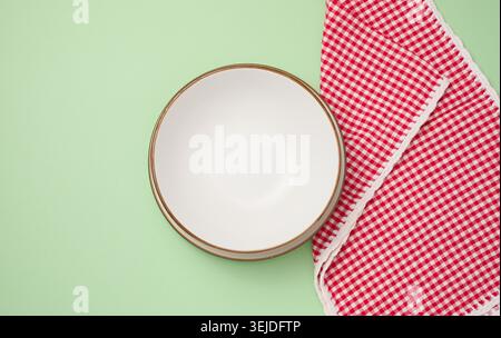 Round ceramic empty white plate and red kitchen towel on green background, top view Stock Photo