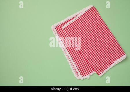 Folded red kitchen towel on a green background, top view. Stock Photo