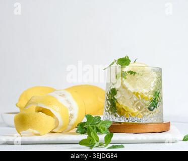 Transparent glass with lemon slices, mint leaves and ice cubes on white table Stock Photo