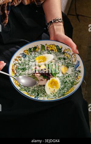Woman holding a decorative bowl of soup with eggs and herbs Stock Photo