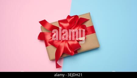 Box wrapped with red ribbon and brown craft paper on a pink blue background, top view Stock Photo