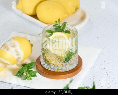 Transparent glass with lemon slices, mint leaves and ice cubes on white table Stock Photo