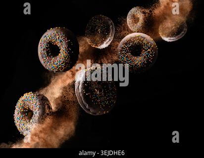 Chocolate donuts with colorful sprinkles levitate on a black background with loose cocoa Stock Photo