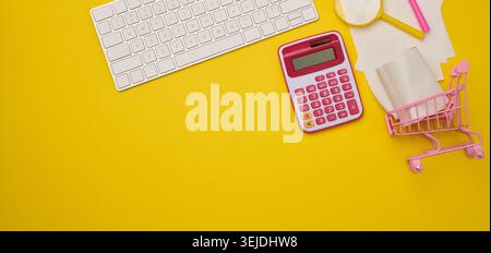 White wireless keyboard, stack of paper receipts and magnifier on yellow background, budget analysis concept, savings Stock Photo