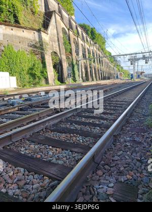 Close-up railway track with overhead power lines in Vienne,France,green-covered wall in background,urban transport,nature contrast Stock Photo