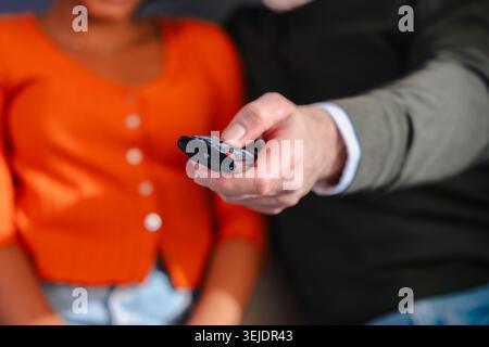 Happy multiracial couple watching television and using remote control on sofa Stock Photo