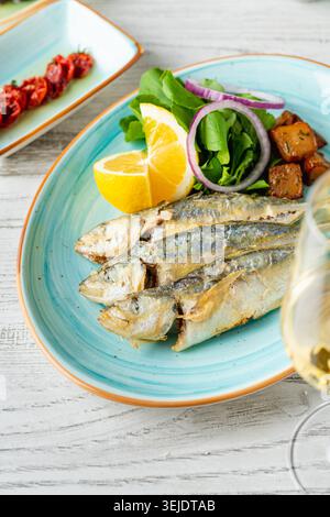 Grilled horse mackerel served with lemon, onion and greens in Mediterranean style presentation Stock Photo
