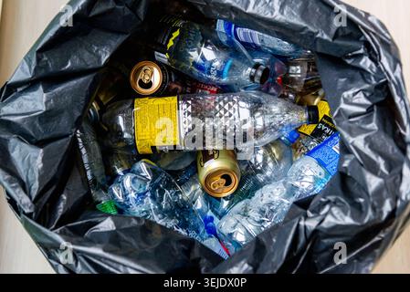 Black garbage bag filled with plastic bottles and cans, showing mixed waste and crumpled plastic texture. Pollution trash disposal, waste management, Stock Photo