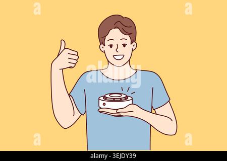 Man with smoke detector gives thumbs up recommending purchase of fire safety equipment. Young guy demonstrating quality smoke detector giving positive Stock Photo