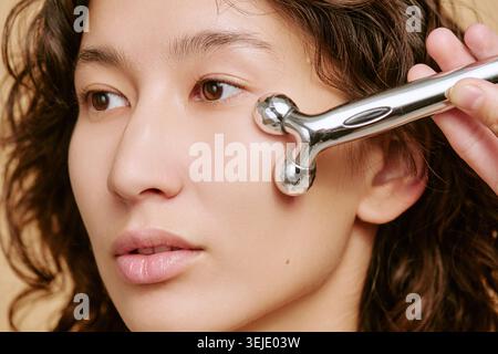 Asian Adult Woman Using Facial Roller for Skincare Routine Stock Photo