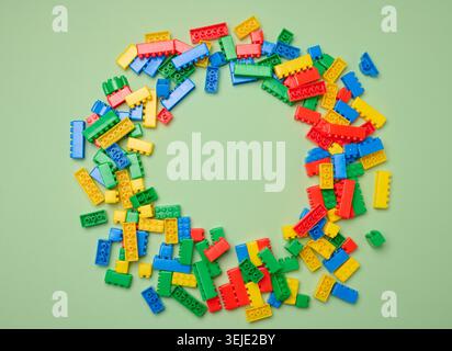 Scattered plastic multi-colored parts of children's construction set on green background, top view Stock Photo