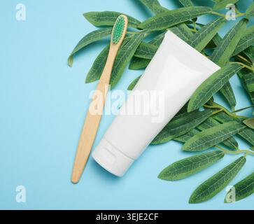 White plastic tube and bamboo toothbrush on blue background, top view Stock Photo