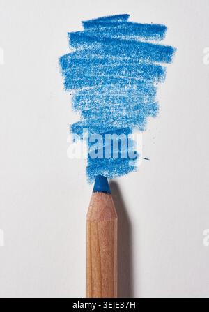 Blue colored pencil with a visible stroke on a white paper surface. The pencil point is facing the stroke, close up Stock Photo