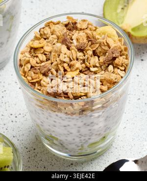 Glass filled with chia seed pudding, layered with diced kiwi at the bottom and topped with crunchy granola Stock Photo