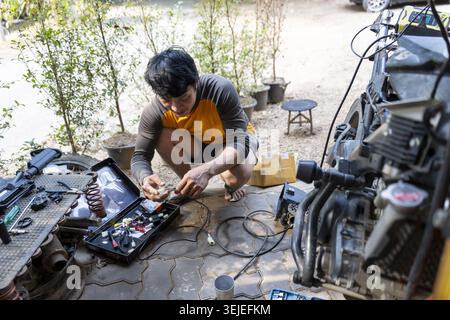 Focused young Asian mechanic man at work, performing repair on an engine in an outdoor workshop. concentrated technician doing technical job with tool Stock Photo