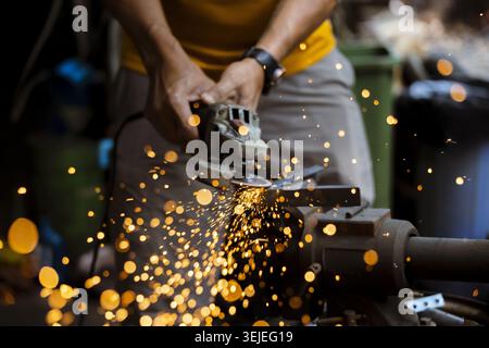 Focused man at work in workshop using power tool. industrial worker grinds metal with an angle grinder, creating shower of bright hot sparks from fric Stock Photo