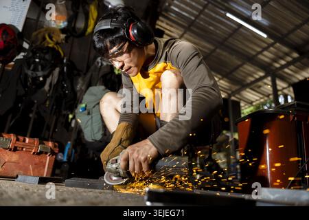 Focused male worker using an angle grinder on metal, creating bright sparks. craftsman wears protective gear in workshop, concentrating on his manual Stock Photo