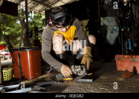 Focused young worker grinding metal with power tool in an outdoor workshop. This craftsman shows intense concentration while using an angle grinder fo Stock Photo