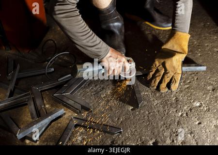 Focused metalworker in workshop using an angle grinder with cutting disc to cut steel. craftsman shows intense concentration while working on metal fa Stock Photo