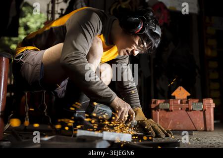 Focused female metalworker in workshop using an angle grinder to cut metal. woman in garage shows intense concentration with sparks flying from power Stock Photo