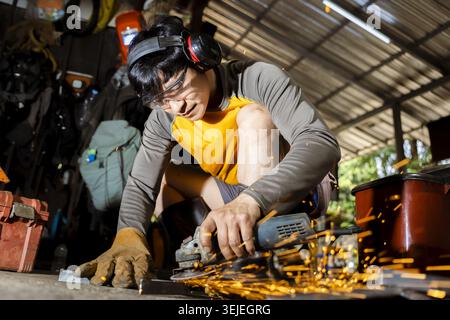 Concentrated man, skilled worker, grinding and cutting metal with power tool. Bright hot sparks fly in workshop. job requires safety equipment and int Stock Photo