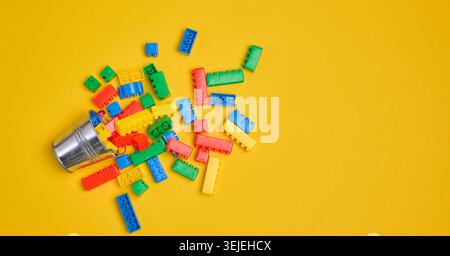 Vibrant colorful building bricks spilling from a silver metal bucket onto a yellow background. Stock Photo