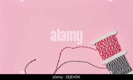 Two spools of red and white and black and white striped twine on a pink background. Stock Photo