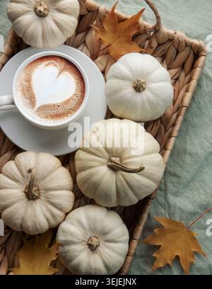 White pumpkins, coffee and autumn leaves on a wicker tray. Stock Photo