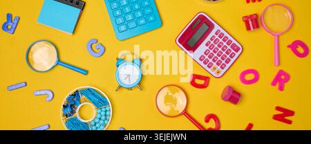 Colorful school supplies, learning items calculators, letters, tools, and stationery scattered on a vibrant yellow background. Stock Photo