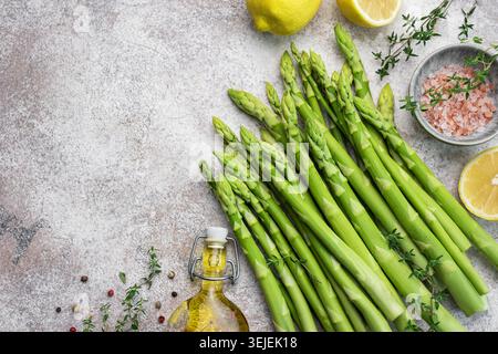 Bunch of raw asparagus stems with different spices on grey concrete background Stock Photo