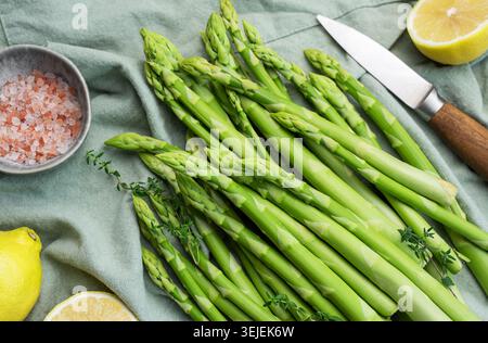 Bunch of raw asparagus stems with different spices on grey concrete background Stock Photo