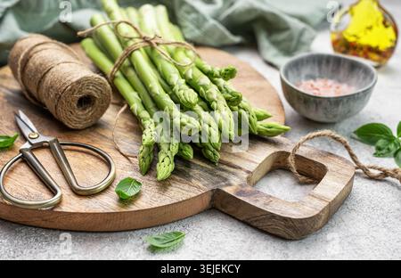 Bunch of raw asparagus stems with different spices on grey concrete background Stock Photo
