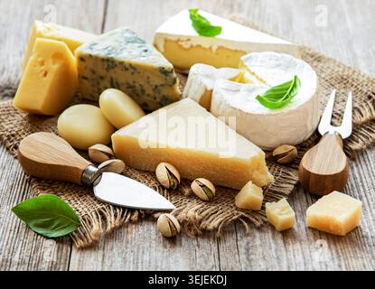 Different types of cheese with basil and nuts on an old wooden table Stock Photo