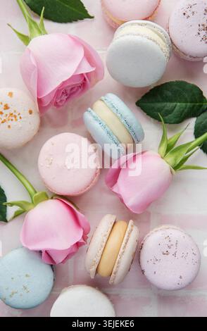 Beautiful colorful tasty macaroons and pink roses on a pink tile background Stock Photo