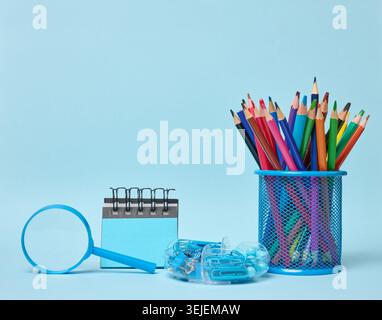 Set of office supplies including colored pencils in a glass, magnifying glass, notepad and paper clips symbolizing learning Stock Photo
