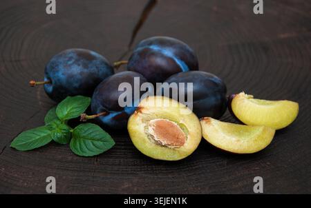 Fresh plums with green leaves on a old black wooden background Stock Photo