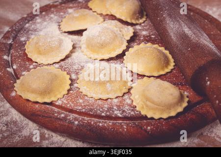 Fresh raw, uncooked ravioli, on a cutting board, with a rolling pin for dough, wooden background, no people, Stock Photo