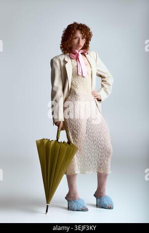 Charming young woman stands confidently in a light outfit, holding a vibrant umbrella with flair. Stock Photo