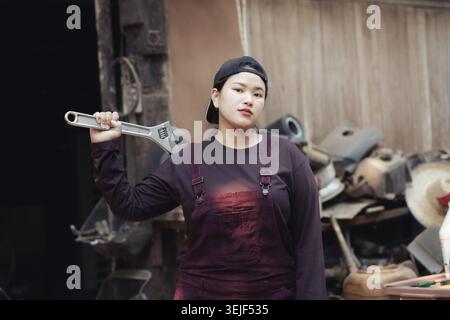 Confident strong woman mechanic holding large wrench in an industrial workshop. This tough worker represents empowerment, posing with determined look Stock Photo