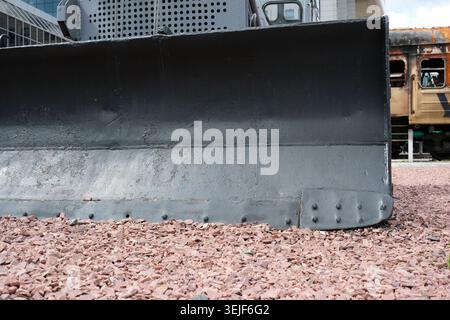 A bulldozer's blade rests on gravel, ready for action in an urban area. Stock Photo