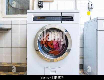 Front view of a white washing machine with a spinning drum and motion blur of colorful laundry Stock Photo