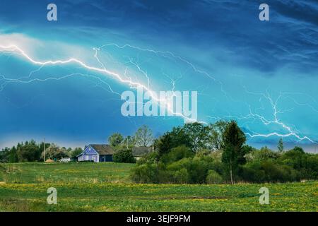 Small Blue House in a Distant Rural Landscape. Lightning Strike Over a Village and Green Field Stock Photo
