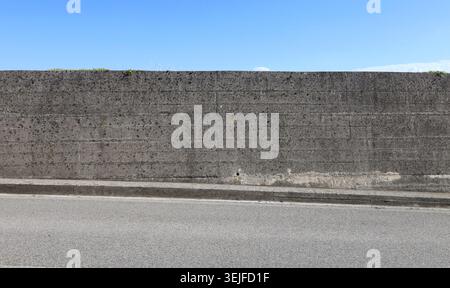 Prefab concrete grunge boundary wall with blue sky above. Sidewalk and street in front. Background for copy space, add text. Stock Photo