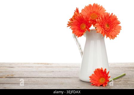 Orange gerbera flowers in pitcher on wooden table. Isolated on white background Stock Photo