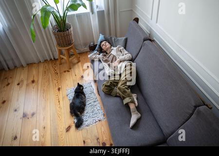 Depressed woman in decline lying half asleep on sofa, motionless with only cat companion for comfort Stock Photo