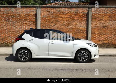 Udine, Italy. May 6, 2023. White and black Toyota Yaris hybrid at the road side. Side view, brick wall on background Stock Photo