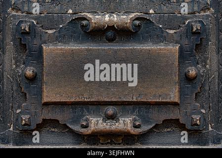 Antique metal plaque with an ornate decorative frame is mounted on a textured wall. Stock Photo