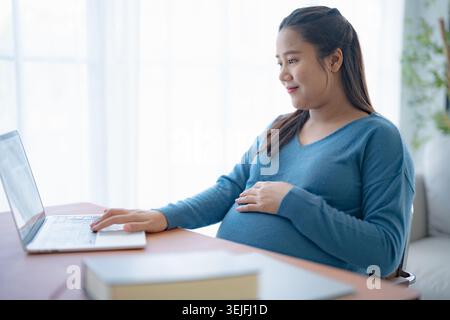 Pregnant asian woman using laptop at home pregnant businesswoman typing on laptop working on remote project in home office pre Stock Photo