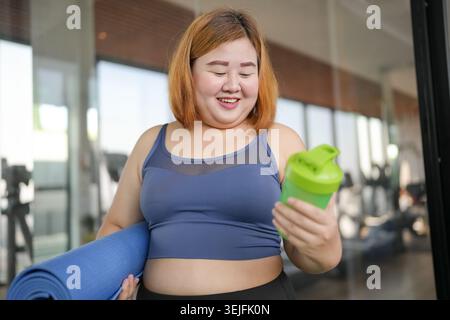 Obese asian woman in sportswear drinking protein shake from bottle After Overweight female exercising for weight loss Energy Vit Stock Photo